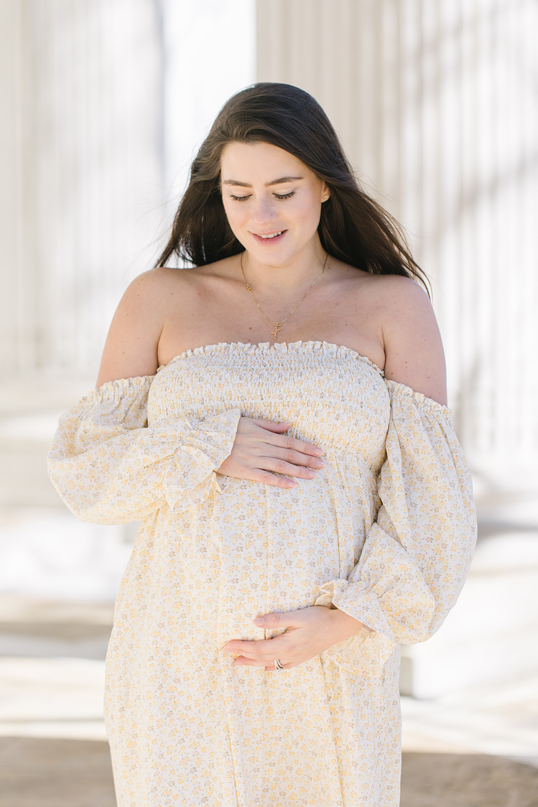 mom to be in cream off the shoulder gown looking down towards her belly Washington DC Prenatal Massage