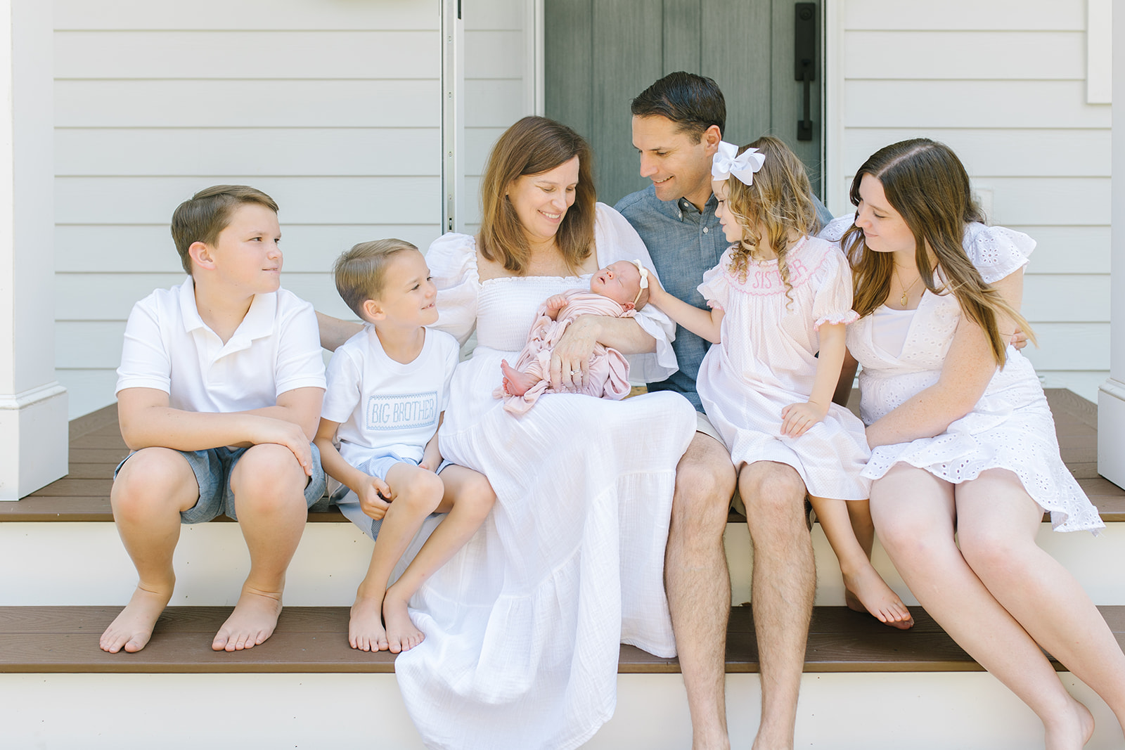 family of 8 sitting on the front porch with a newborn baby