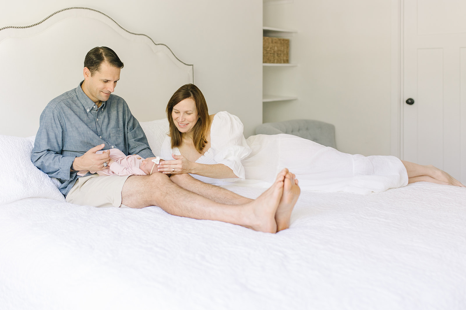 mom and dad laying on a white bed with holding their newborn Northern Virginia Newborn Photographer