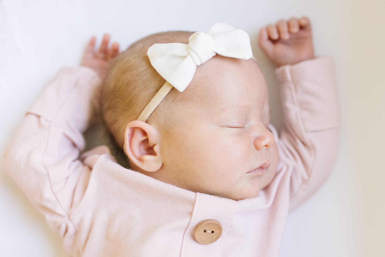 baby girl in pink onesie and white bow sleeping with her arms up Northern Virginia Newborn Photographer