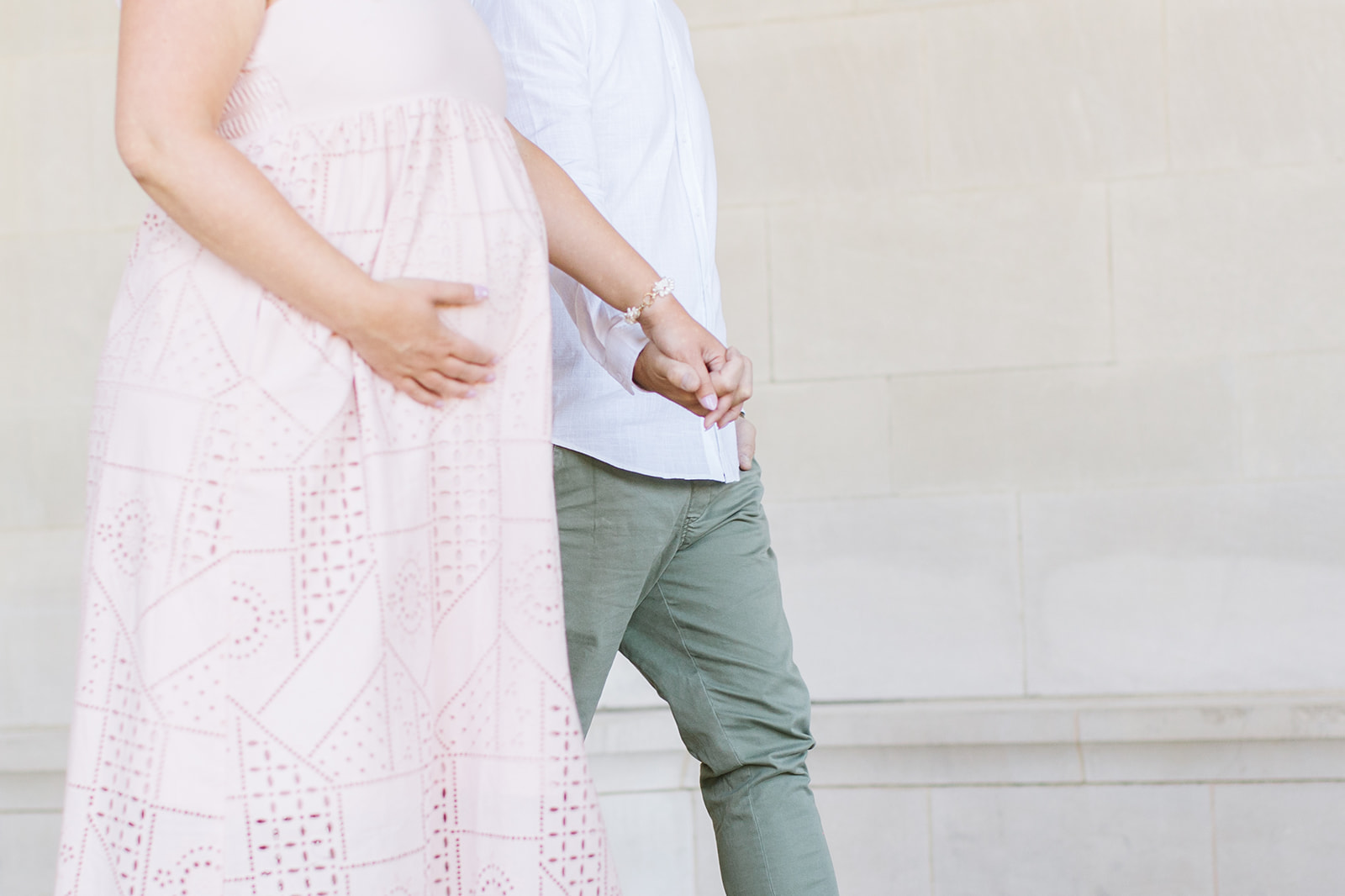 close up of couple walking with one hand on a baby bump