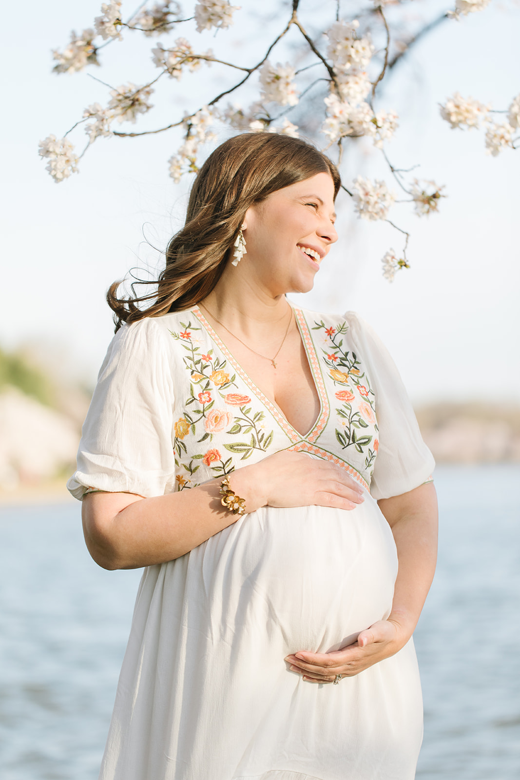 pregnant woman in white floral gown laughing during cherry blossom season Maternity Photography DC