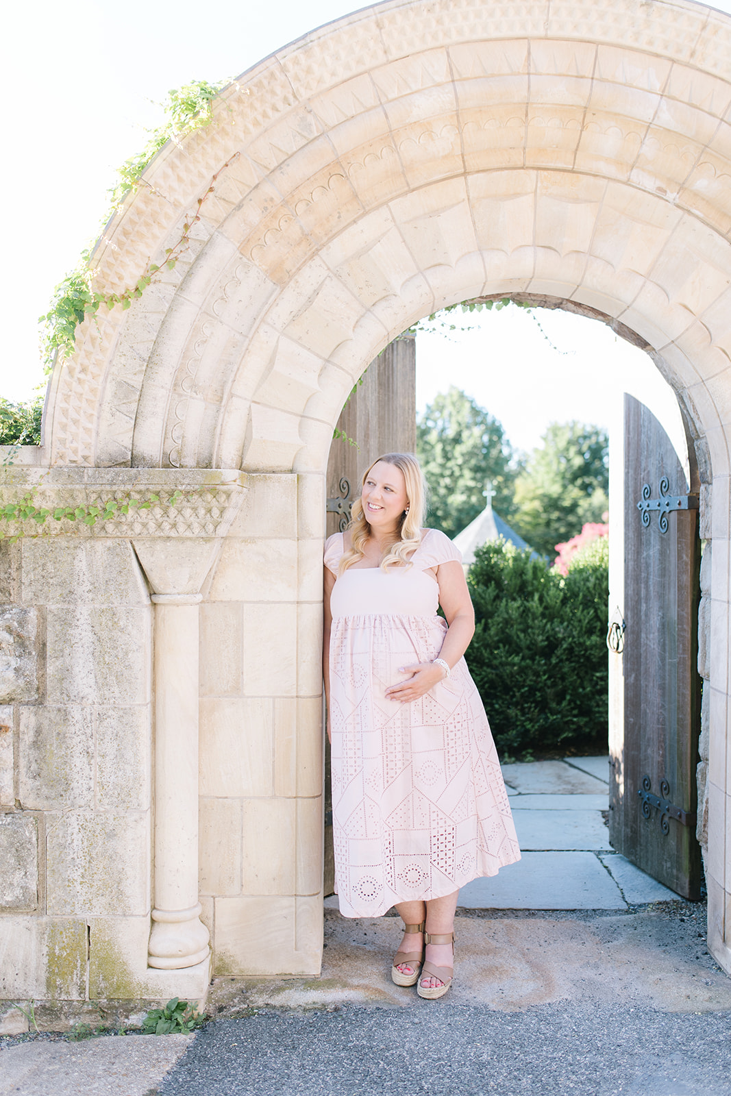 Mom to be in pink dress leaning against a column in DC
