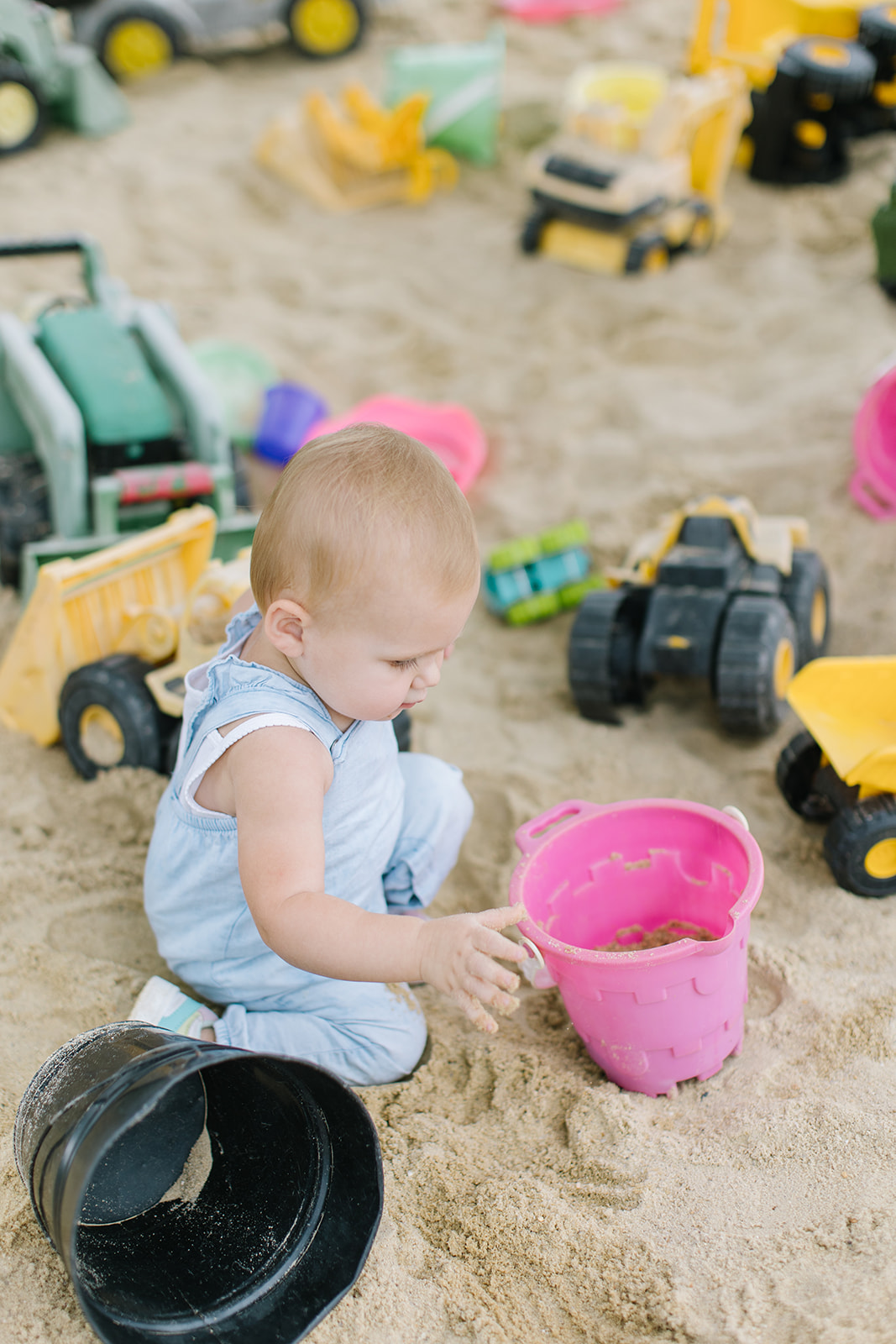 child playing in the sand with trucks and a bucket