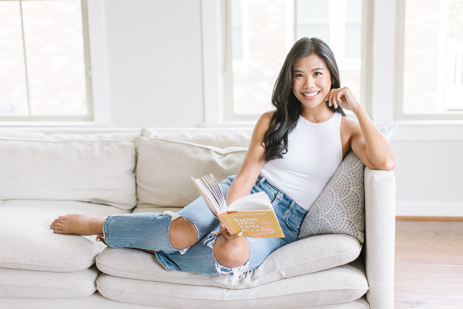 woman in white tank top and ripped jeans reading a book on a grey couch Personal Branding Washington DC