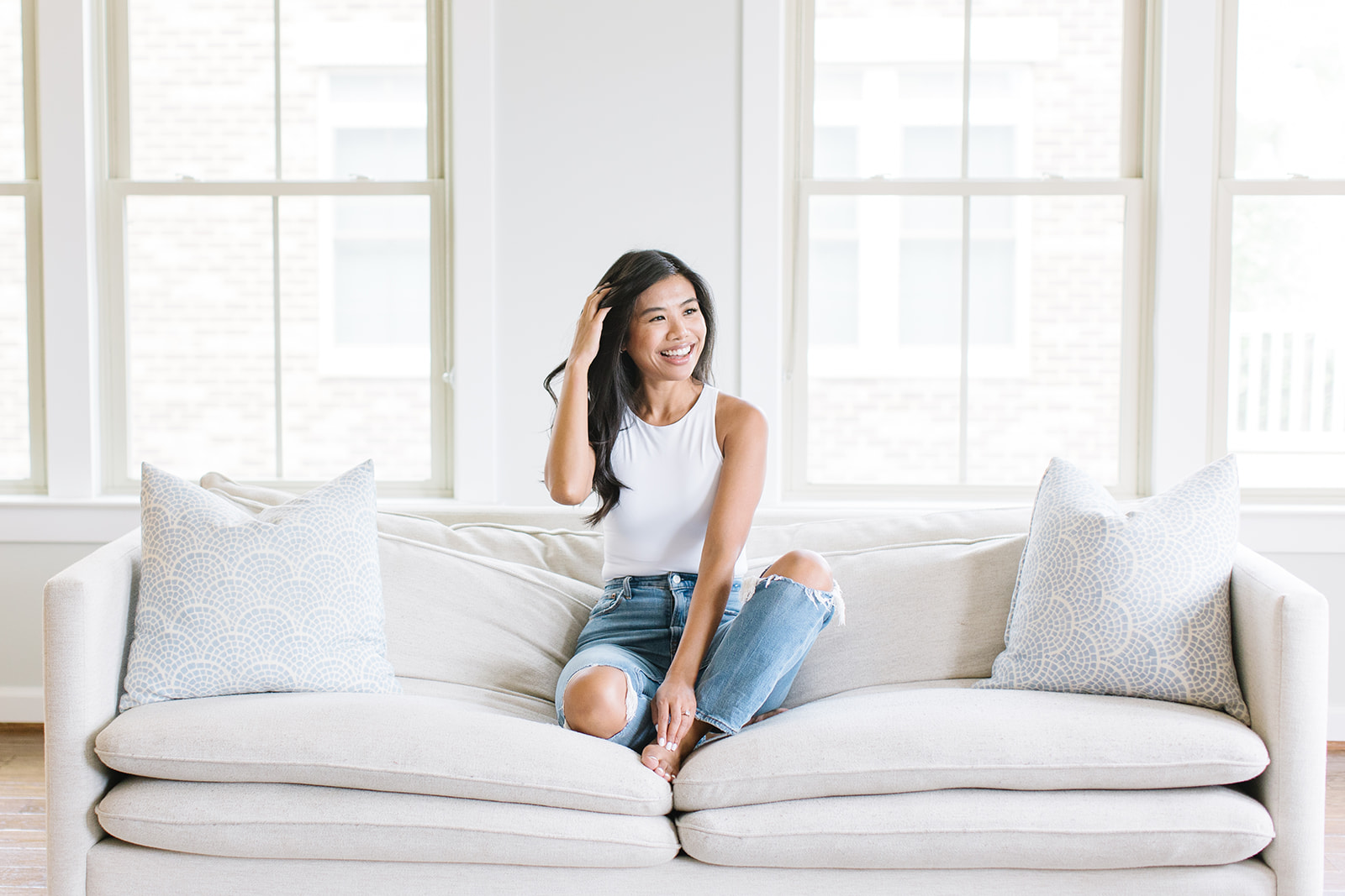 woman in a white sleeveless shirt and ripped jeans with her hand in her hair sitting on a couch Personal Branding Washington DC