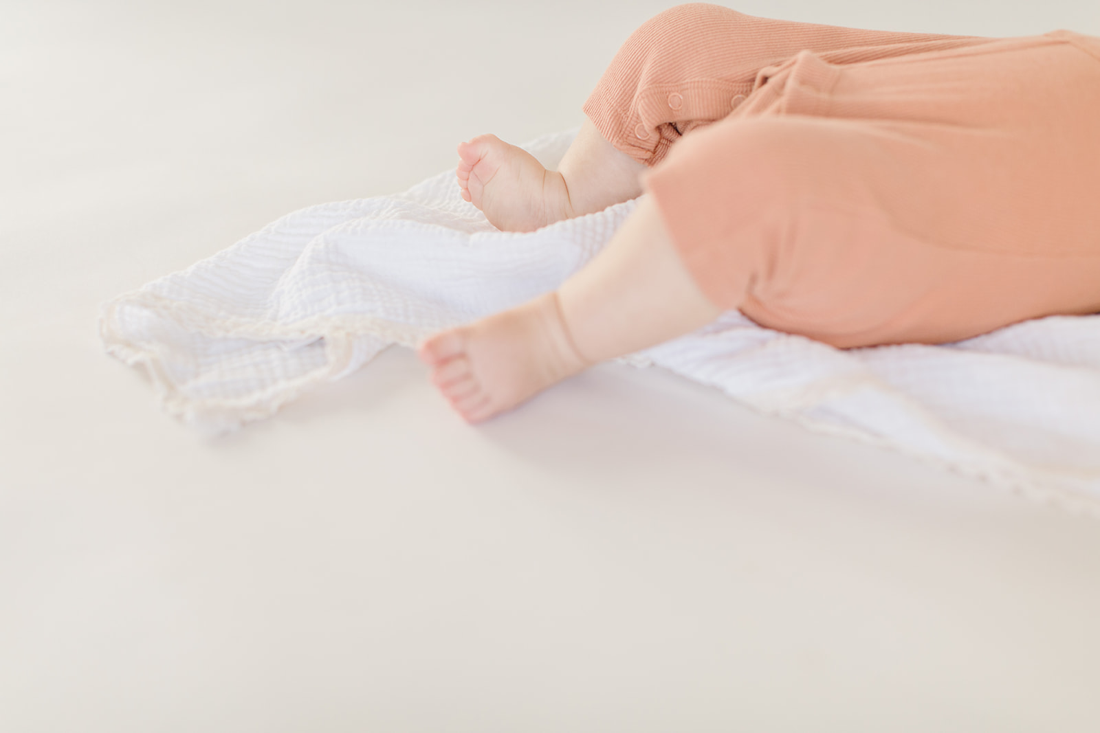 newborn baby in an orange onesie lays on a white blanket in a studio