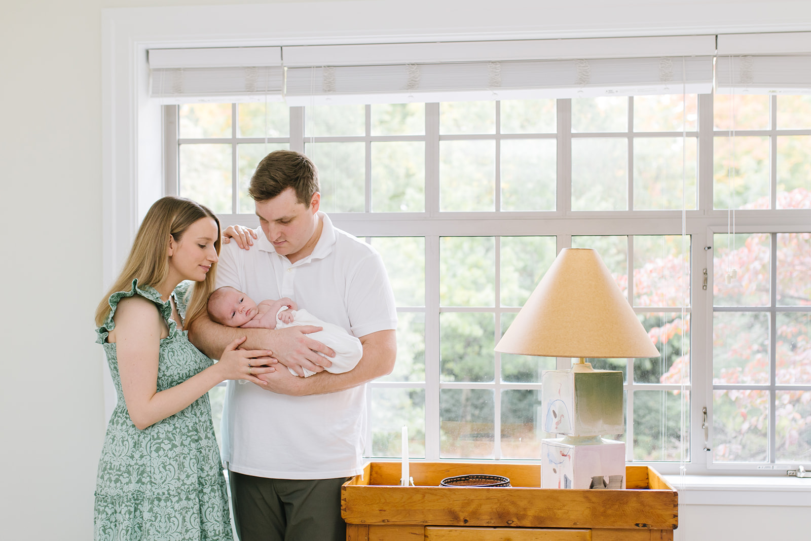 new parents hold their newborn in front of a large window and wooden table interior design washington dc