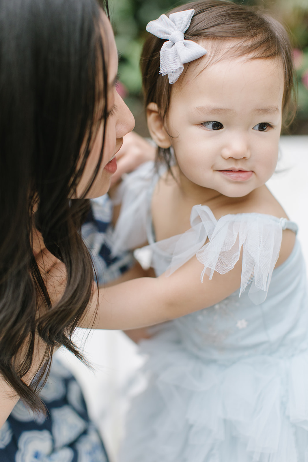 mom tries to kiss her toddler daughter in a blue dress but is pushed away