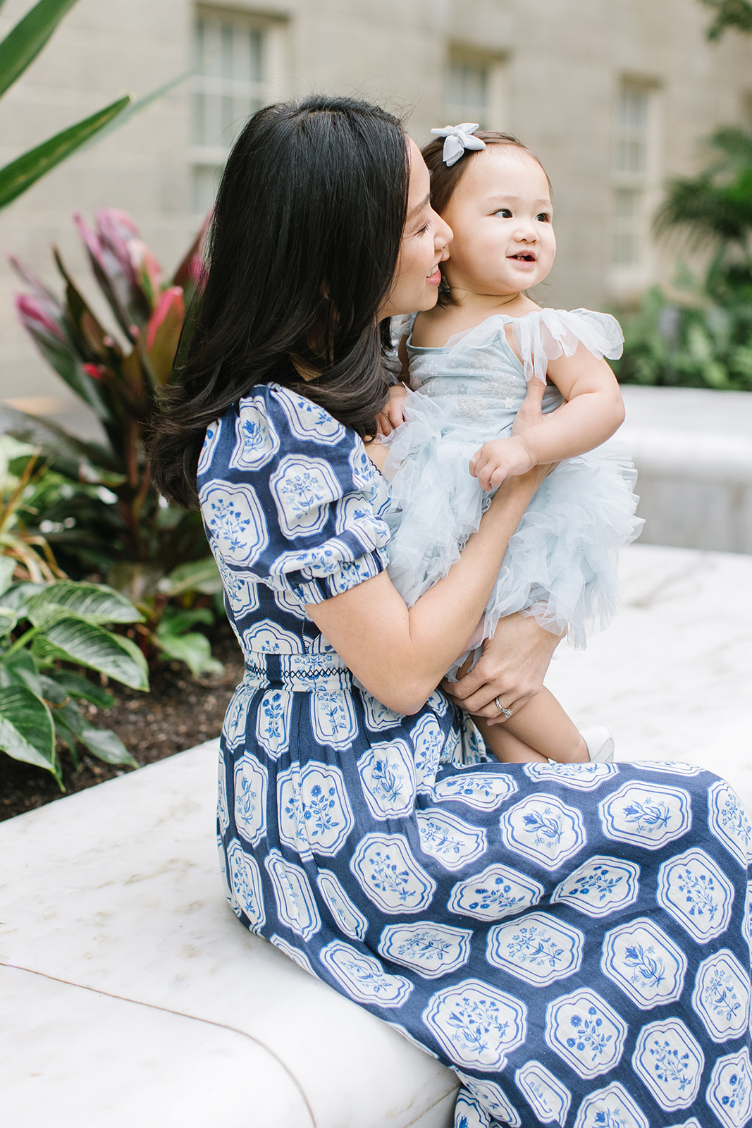 mom in a blue and white patterned dress sit on a garden bench with her toddler daughter in a drress Mommy and me classes DC