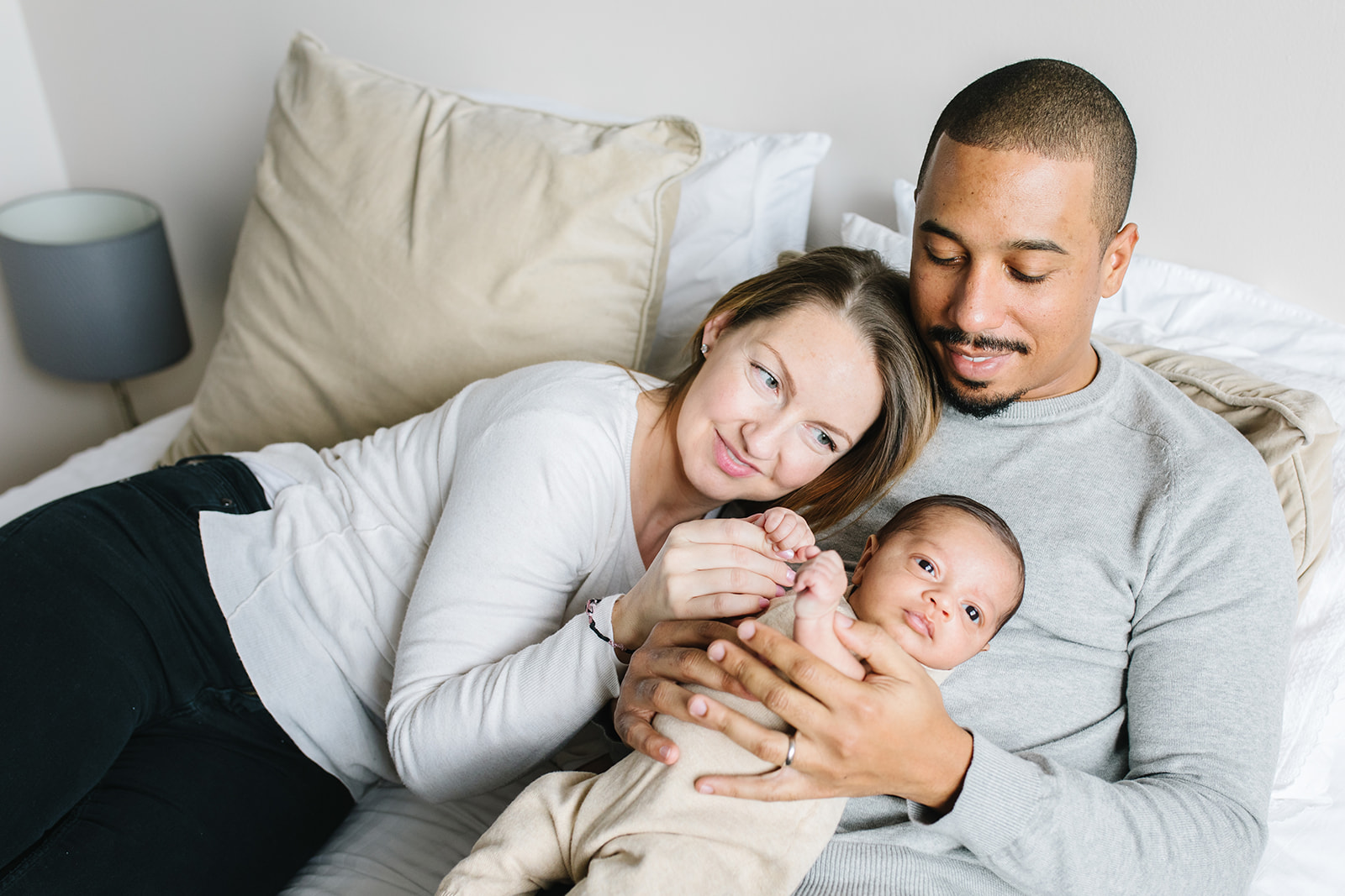 mom and dad cuddle with their newborn child laying on dad in bed parenting classes in DC