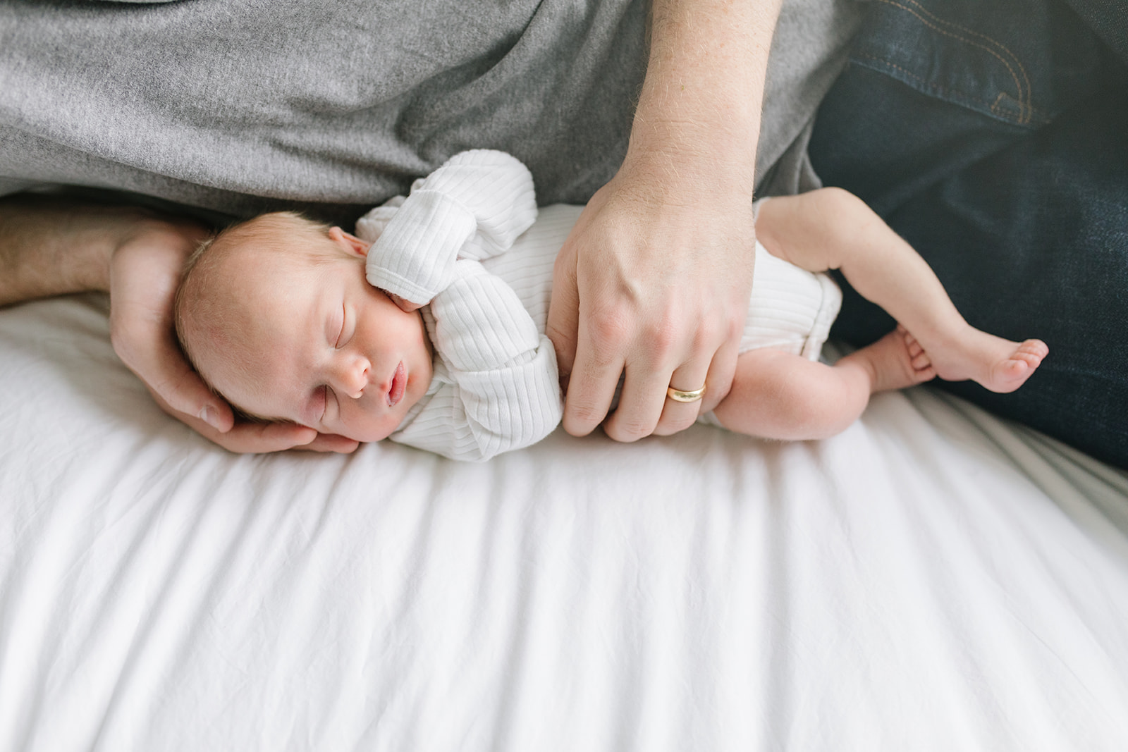 dad in grey shirt lays and cuddles his newborn child on a bed